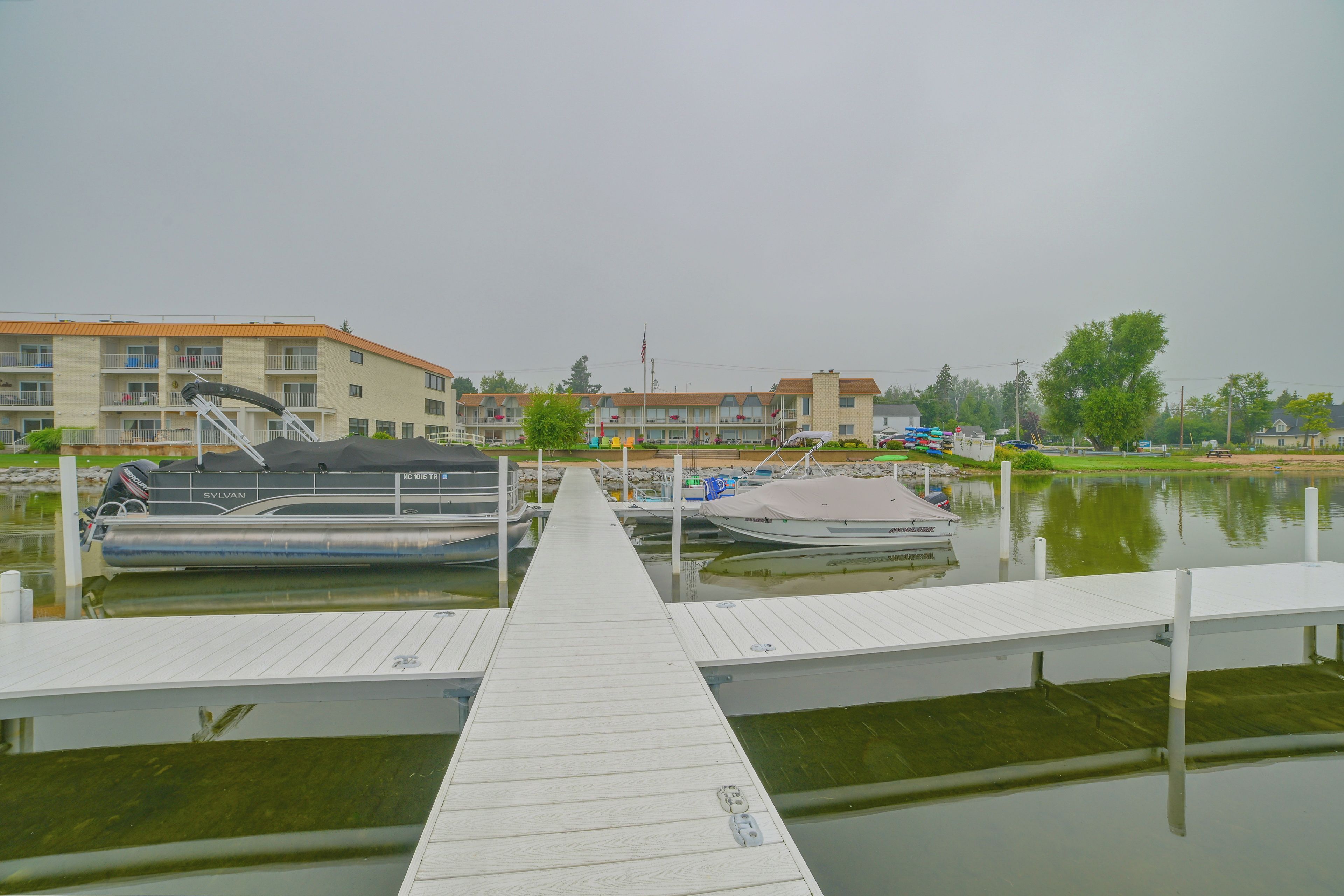 A marina with docked boats, a wooden pier, and buildings in the background.