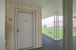 A door with a metal handle, a brick wall, and a view of a green lawn with outdoor furniture. - Lakefront Studio, 3 Mi to Petoskey State Park! (Conway)