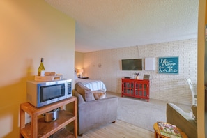 A cozy living room with a sofa, a red cabinet, a television, and a microwave on a wooden stand. - Lakefront Studio, 3 Mi to Petoskey State Park! (Conway)