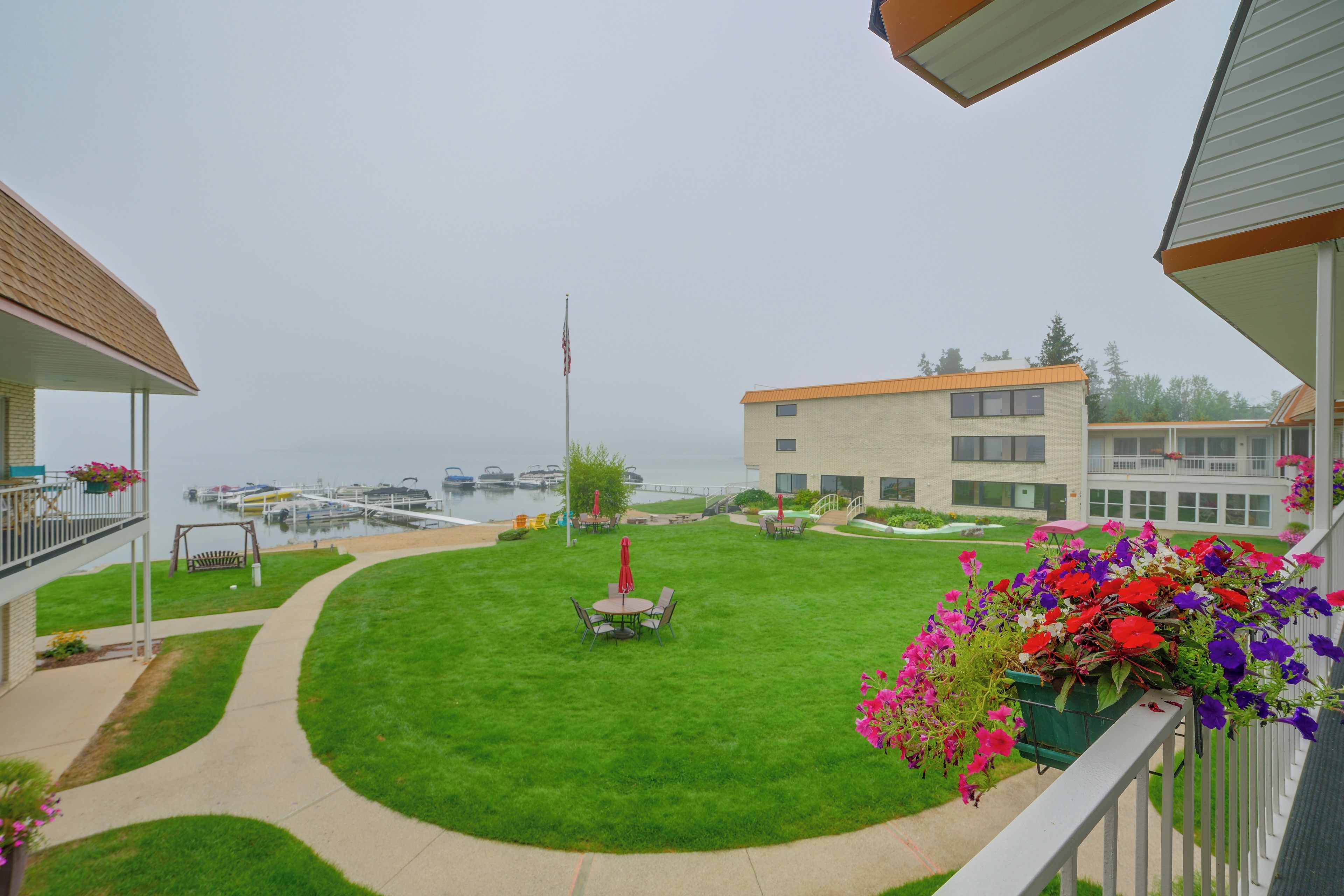 Un barrio residencial con un césped bien cuidado, un patio con mobiliario exterior y vistas al puerto deportivo con barcos.