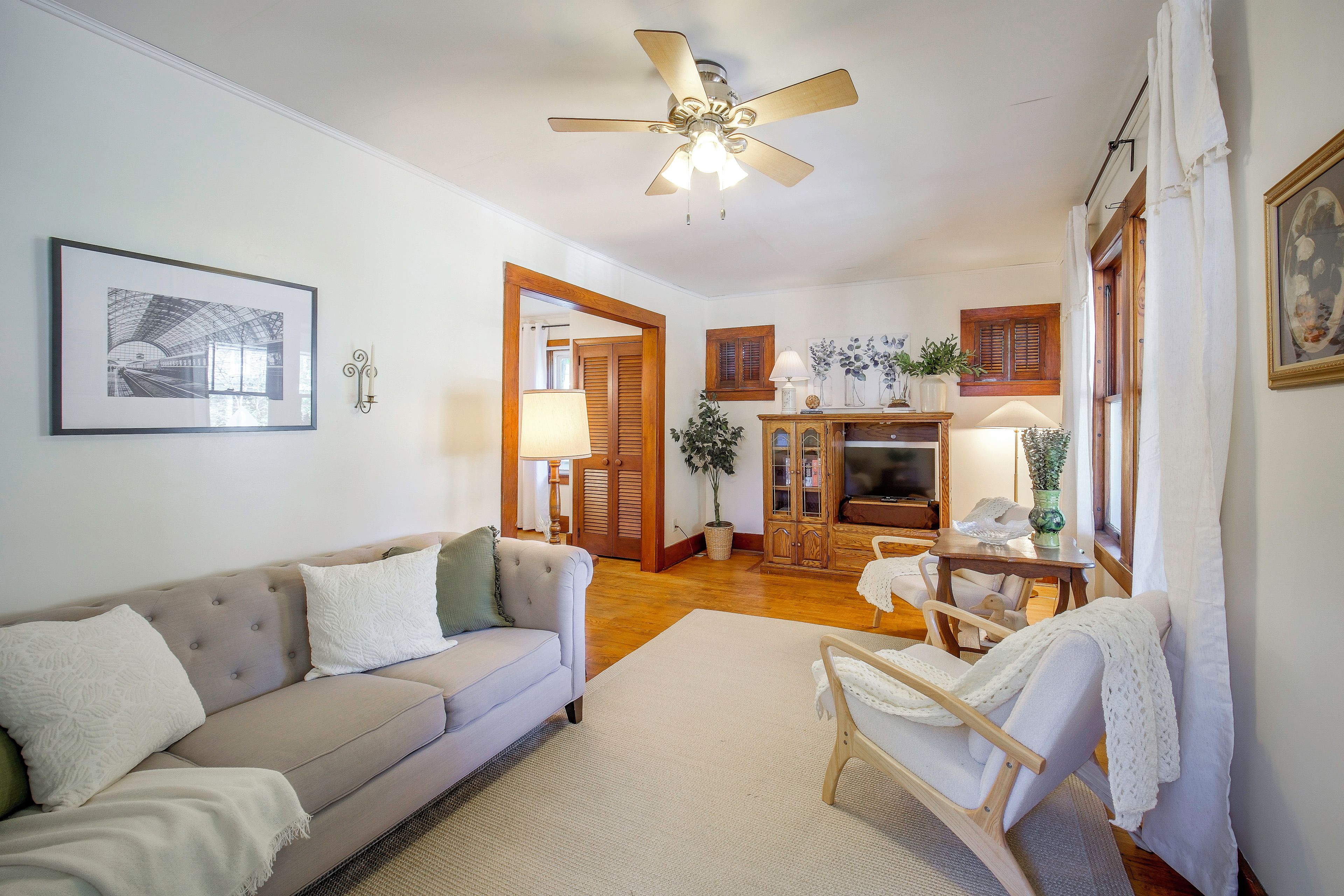 A living room with a sofa, a wooden cabinet, a television, and a ceiling fan.