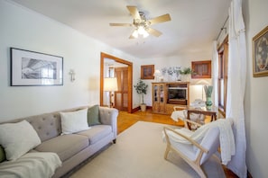 A living room with a sofa, a wooden cabinet, a television, and a ceiling fan. - Hot Tub Haven in Wooster: Walk to Shops & Eats! (Wooster)