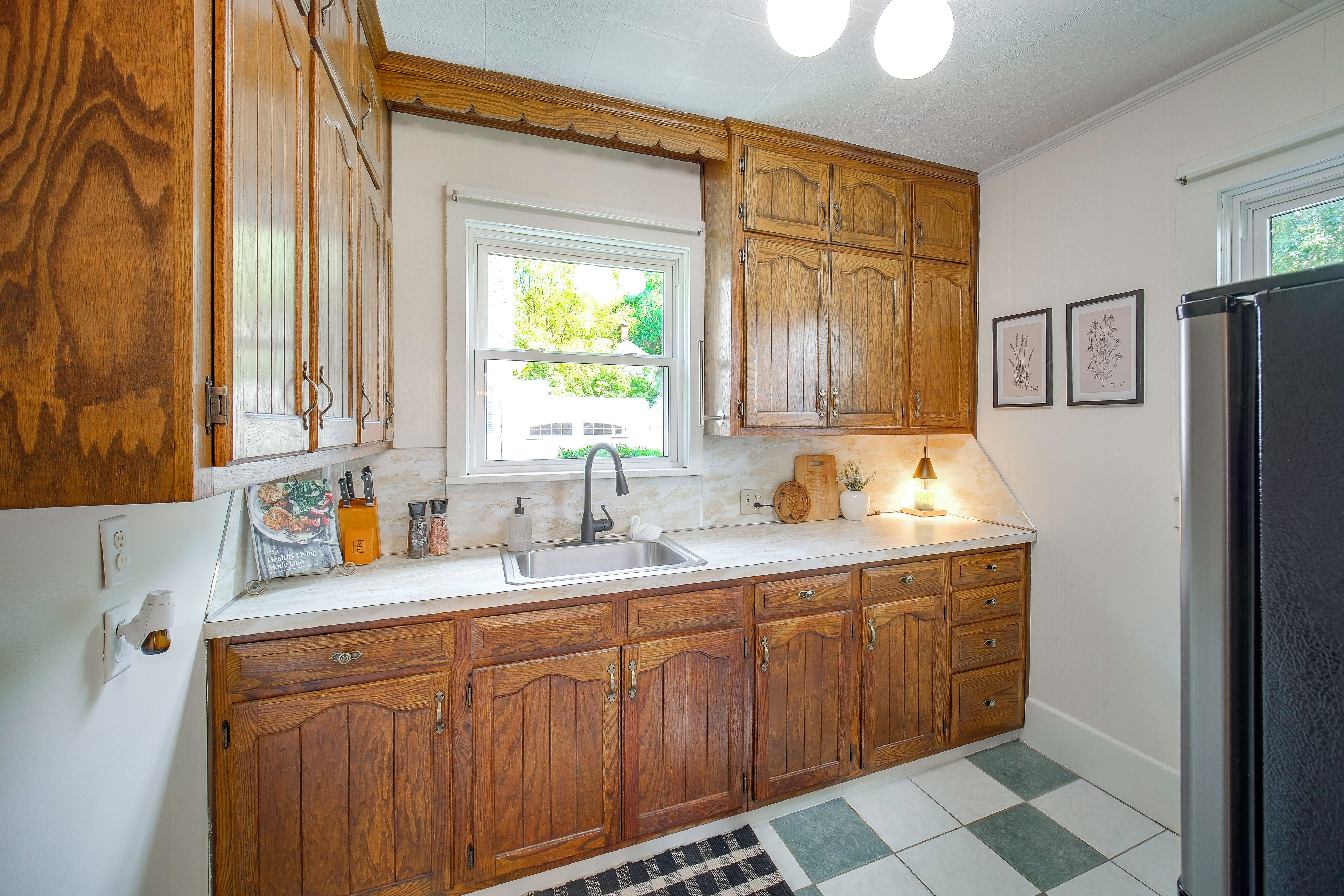 A kitchen with wooden cabinets, a sink, a window, and a refrigerator.