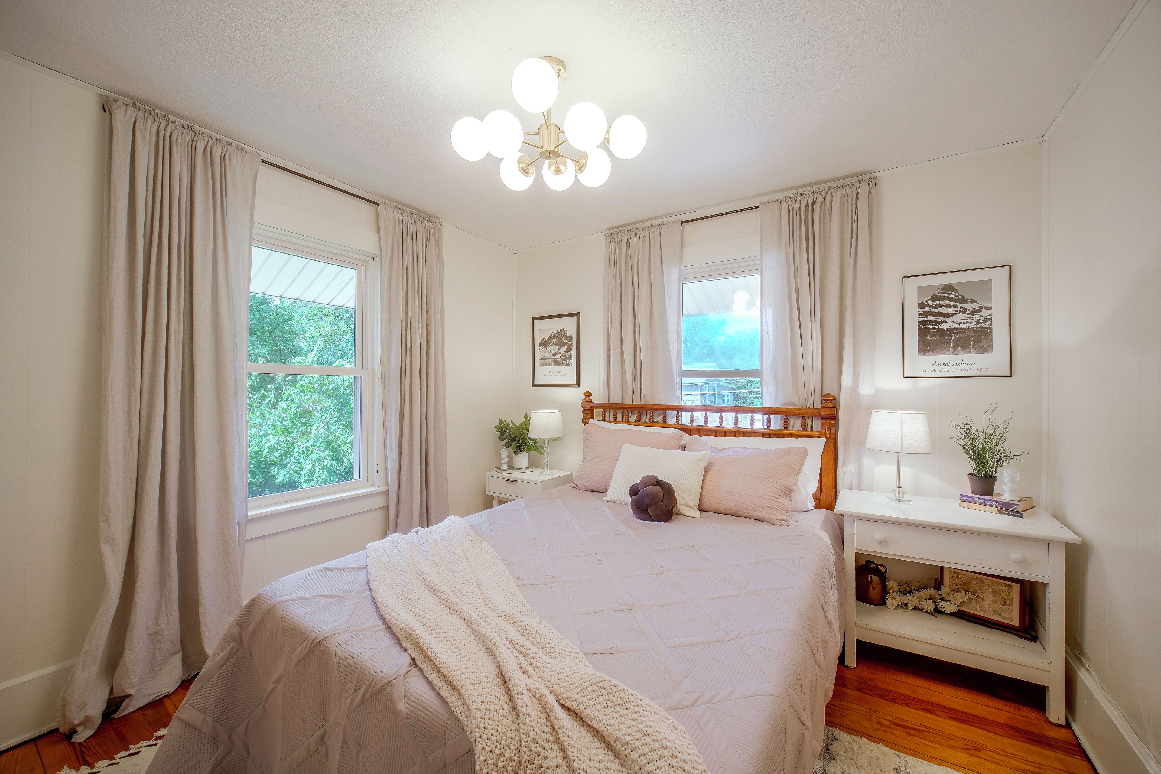 A bedroom with a bed, bedside tables, a nightstand, a lamp, a framed picture, and a window with curtains.