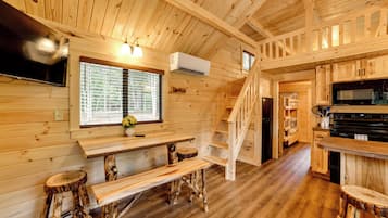 A wooden cabin interior with a kitchen, dining area, and a staircase.