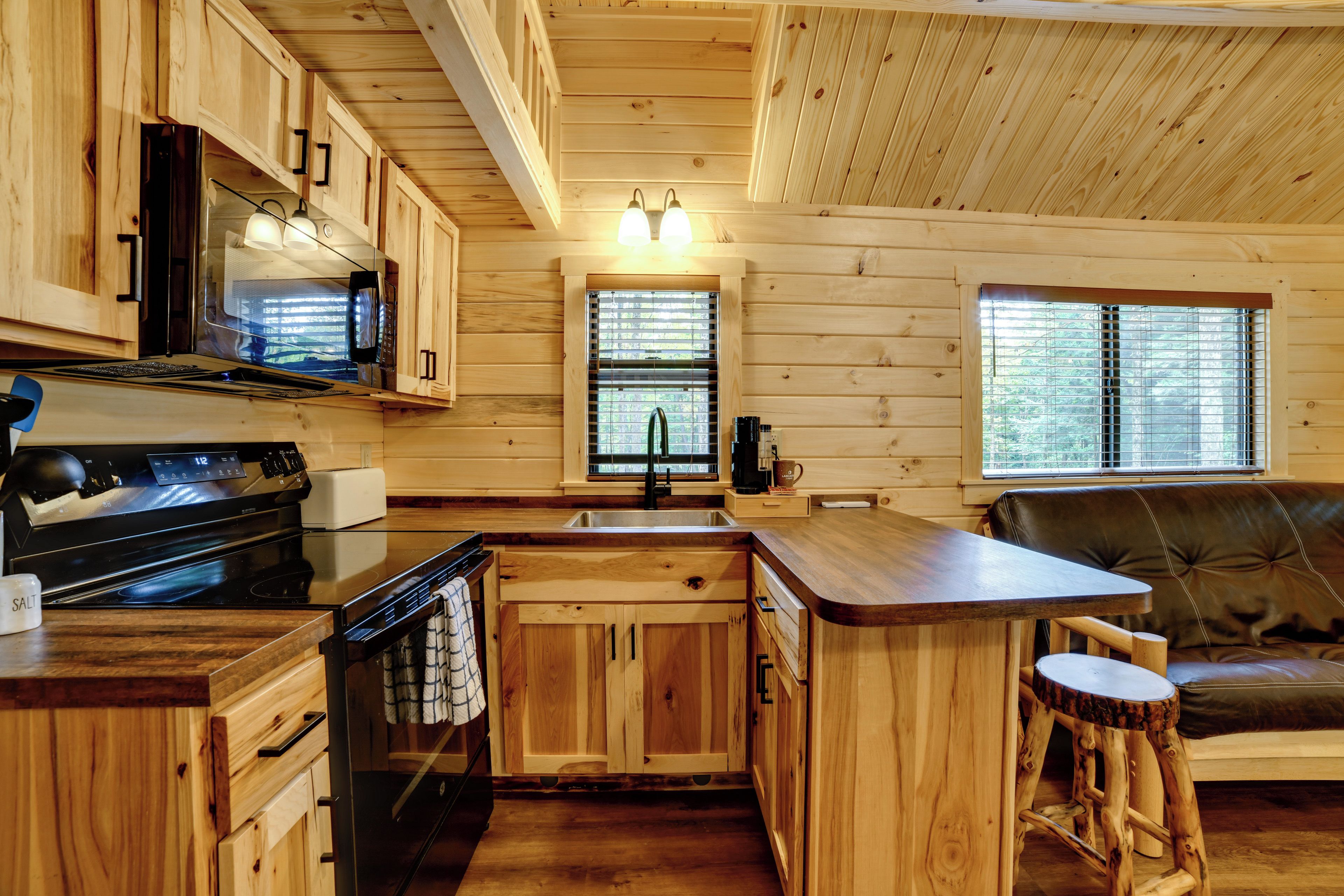 A wooden cabin interior with a kitchen, dining area, and a window with blinds.