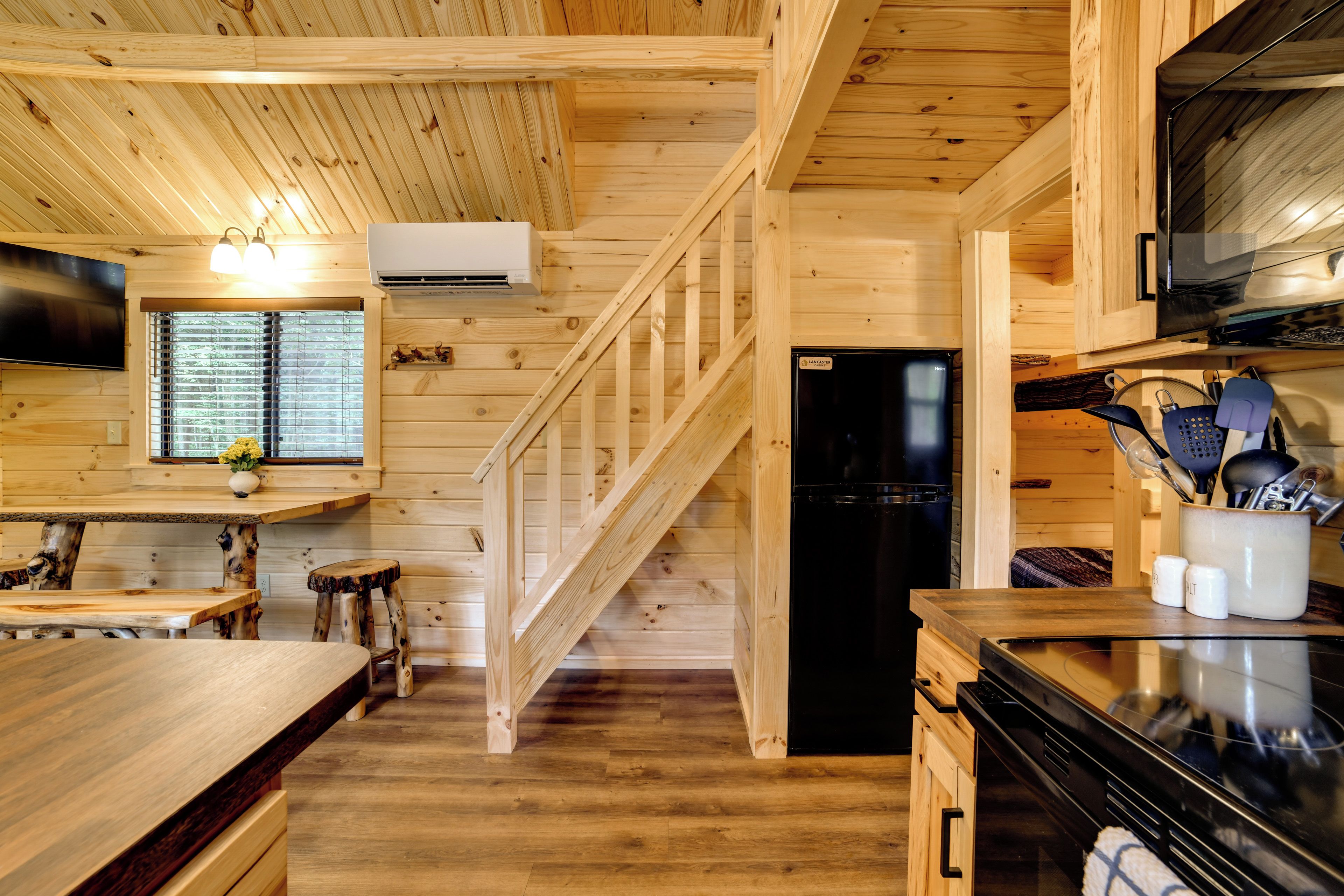 A wooden interior with a kitchen area, including a refrigerator, stove, and wooden flooring.