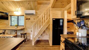 A wooden interior with a kitchen area, including a refrigerator, stove, and wooden flooring.