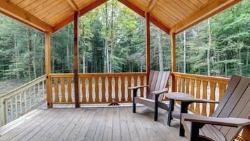 A wooden deck with a covered area, two chairs, and a table.