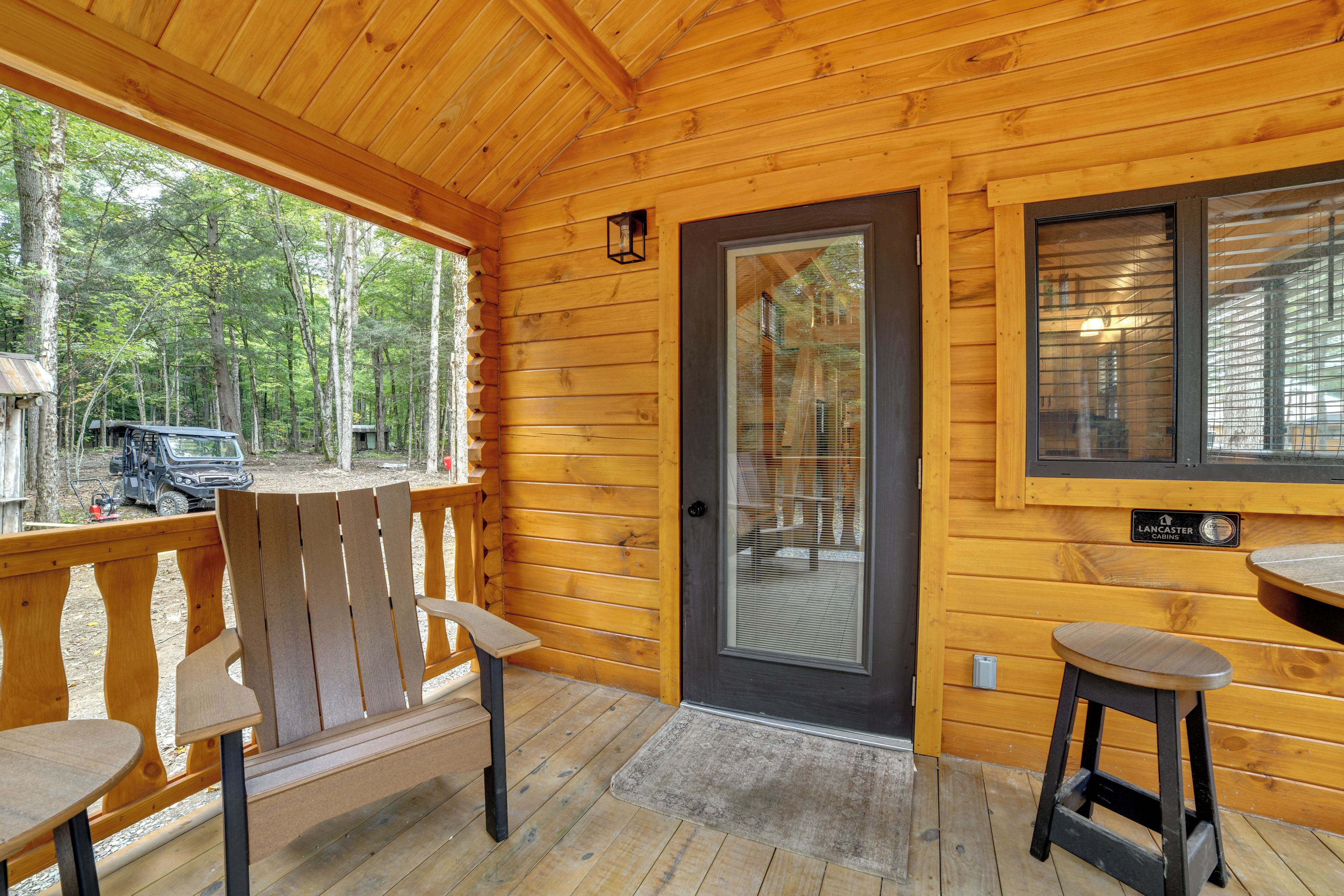 A wooden cabin with a porch, two chairs, a table, and a door with a window.