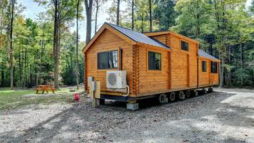 A log cabin with a metal roof, a small porch, and a picnic table in a forested area.