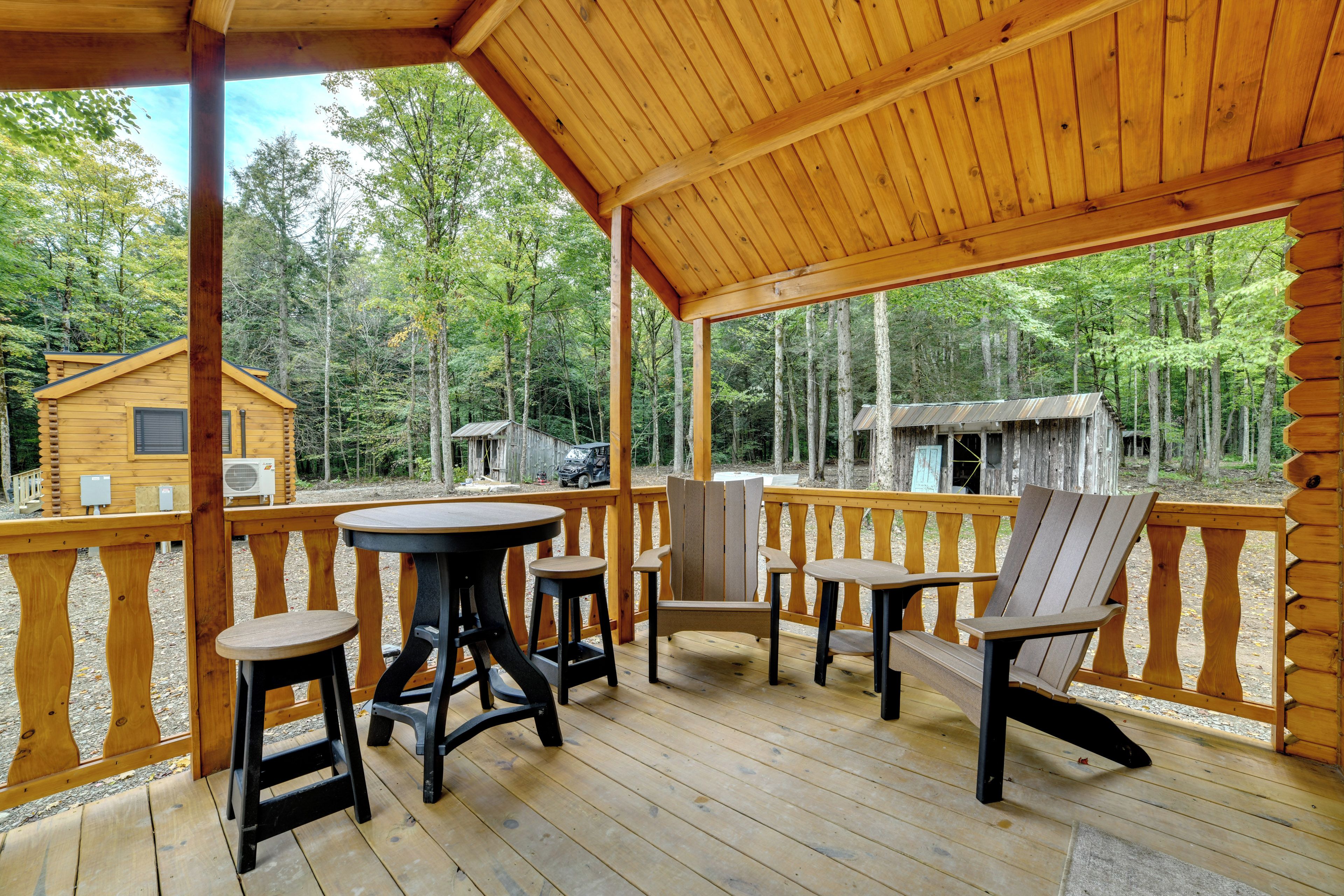 A wooden deck with a table and chairs, overlooking a forested area with cabins.