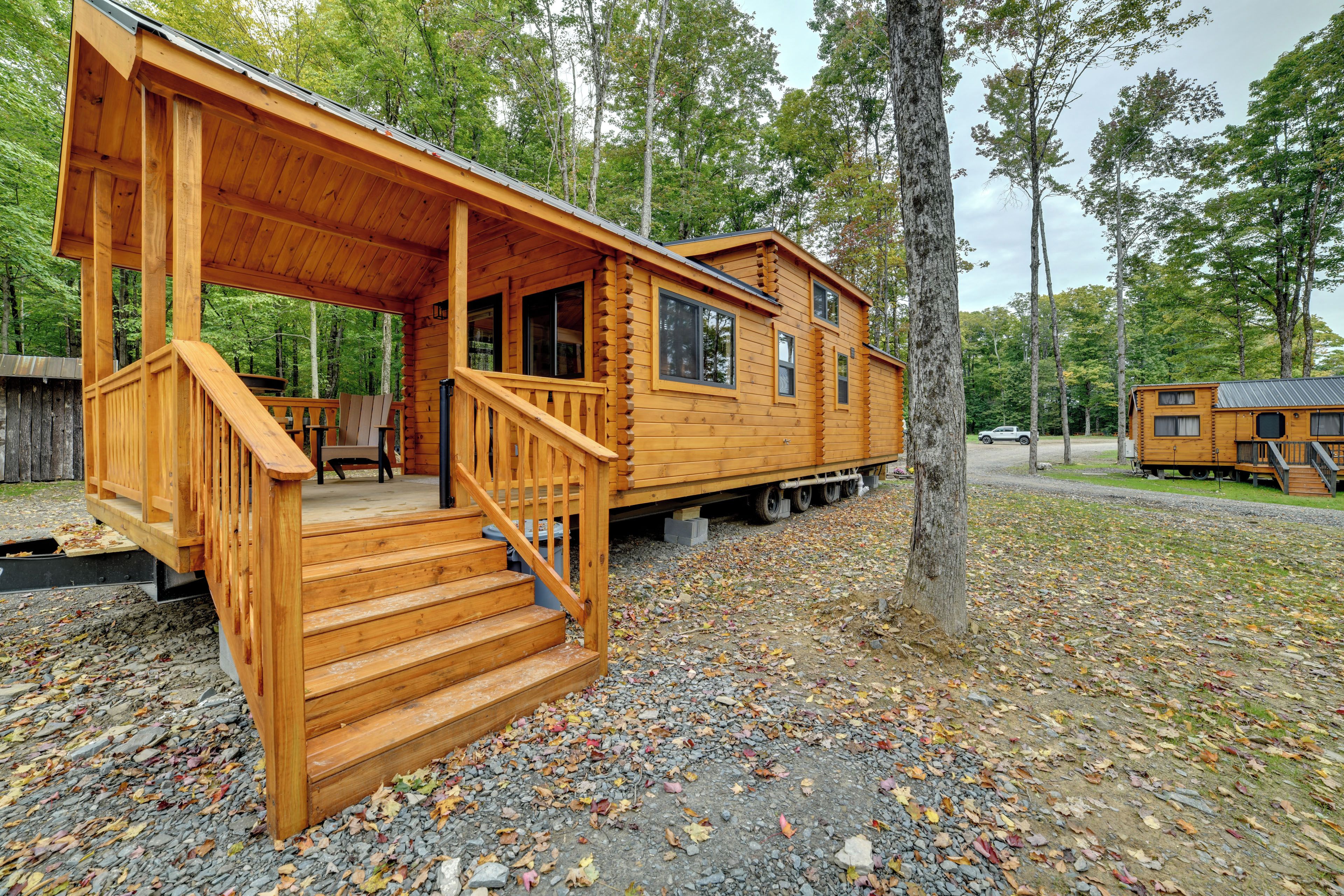 A wooden cabin with a porch and stairs, surrounded by trees and gravel ground.