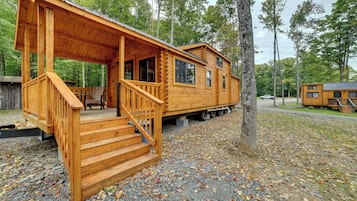 A wooden cabin with a porch and stairs, surrounded by trees and gravel ground.