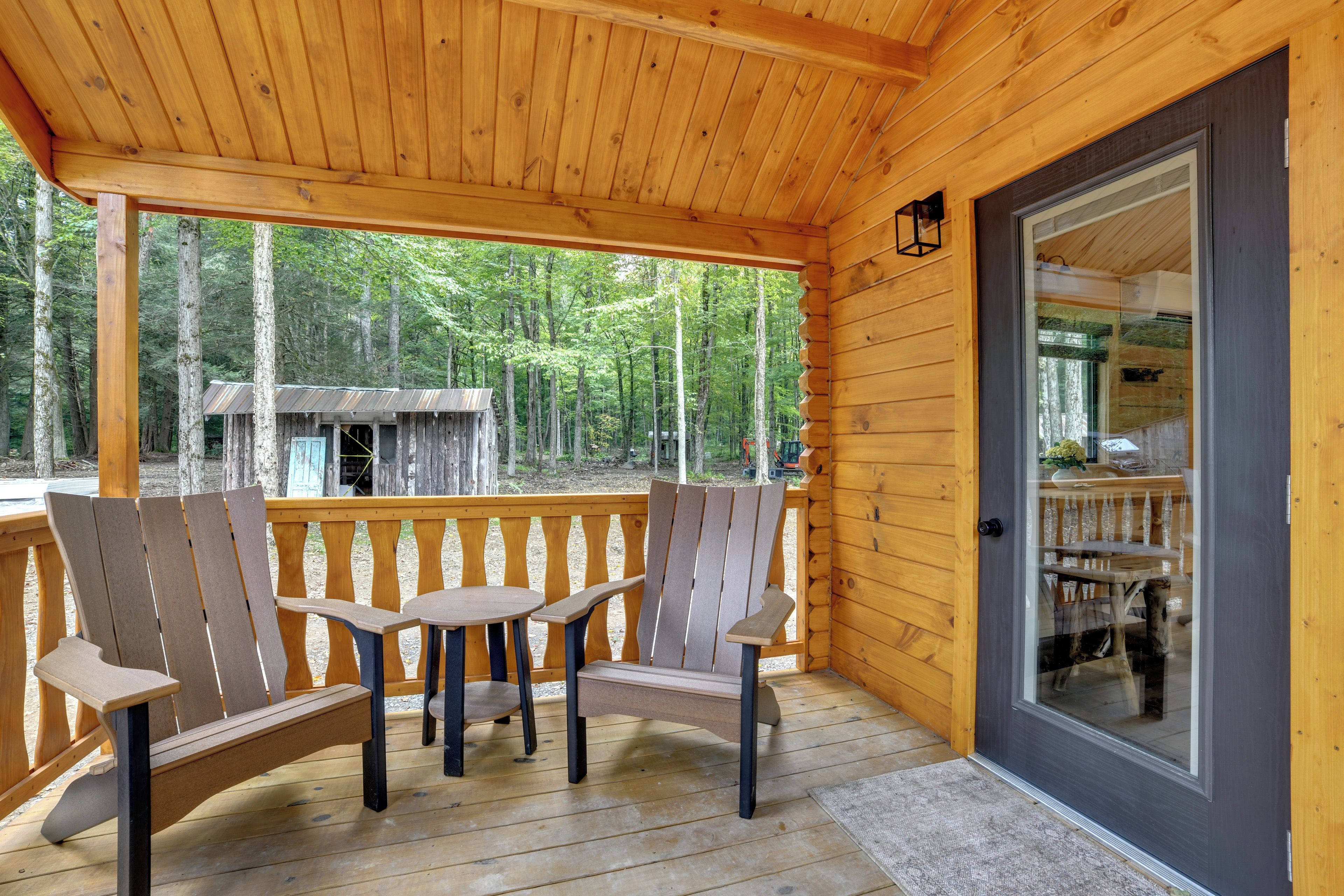 A wooden deck with Adirondack chairs and a table, overlooking a forested area.