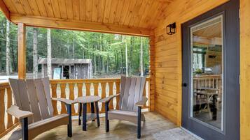 A wooden deck with Adirondack chairs and a table, overlooking a forested area.
