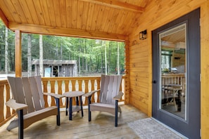 Una terraza de madera con sillas Adirondack y una mesa, con vistas a una zona boscosa.