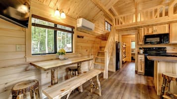A wooden cabin interior with a kitchen, dining area, and a staircase leading to an upper level.