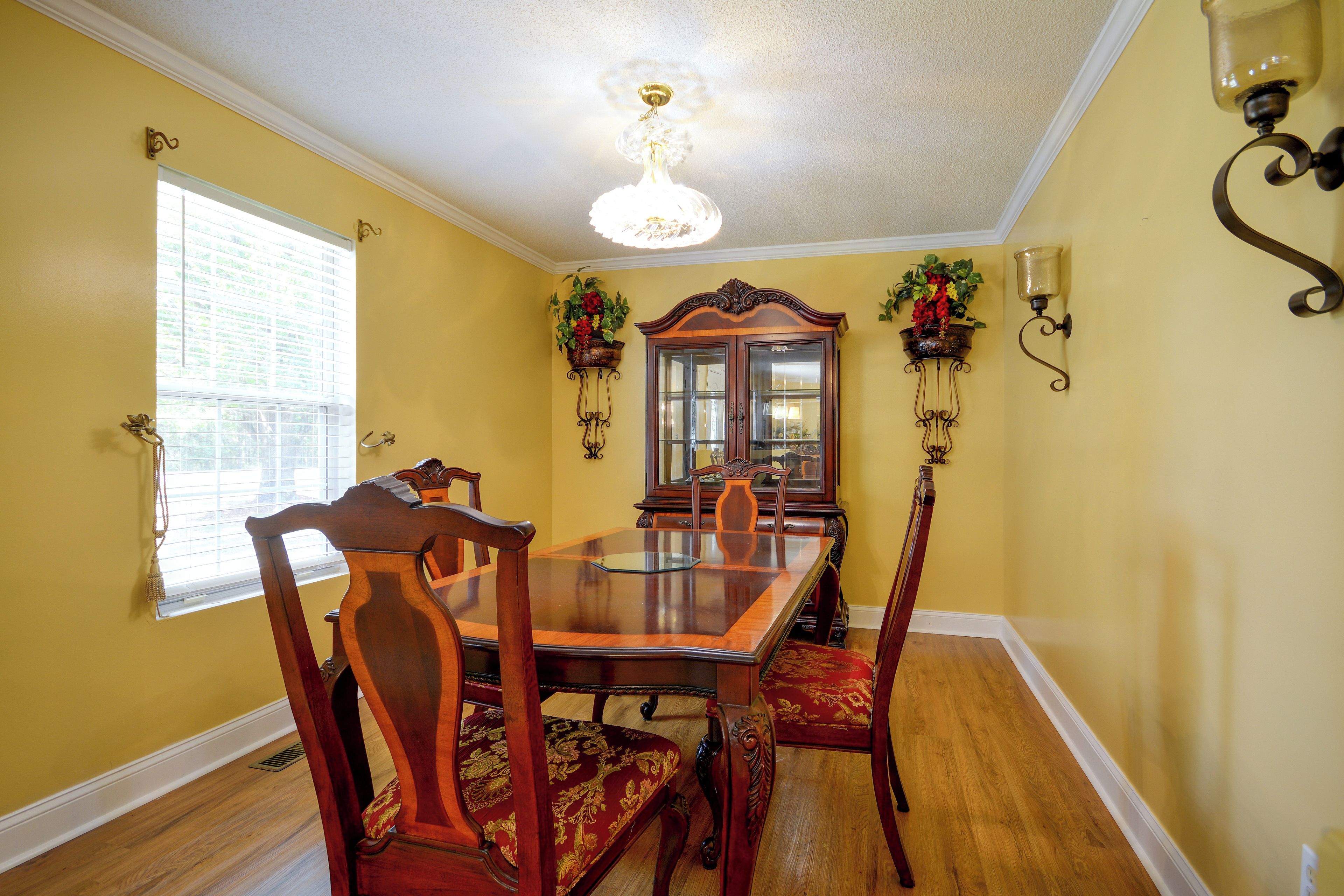 A dining room with a wooden table and chairs, a chandelier, and wall-mounted sconces.