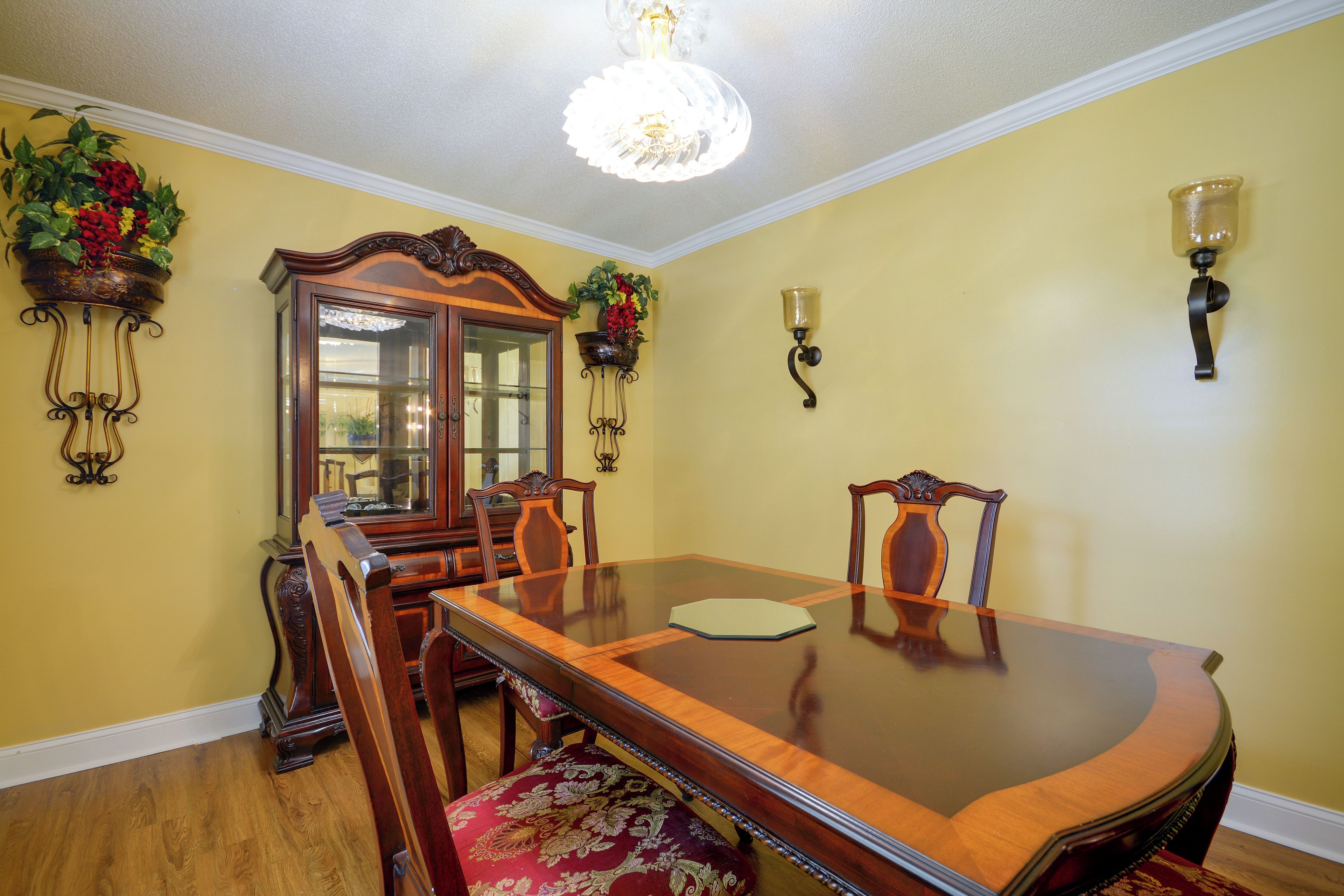 A dining room with a wooden table, chairs, a chandelier, and wall-mounted sconces.