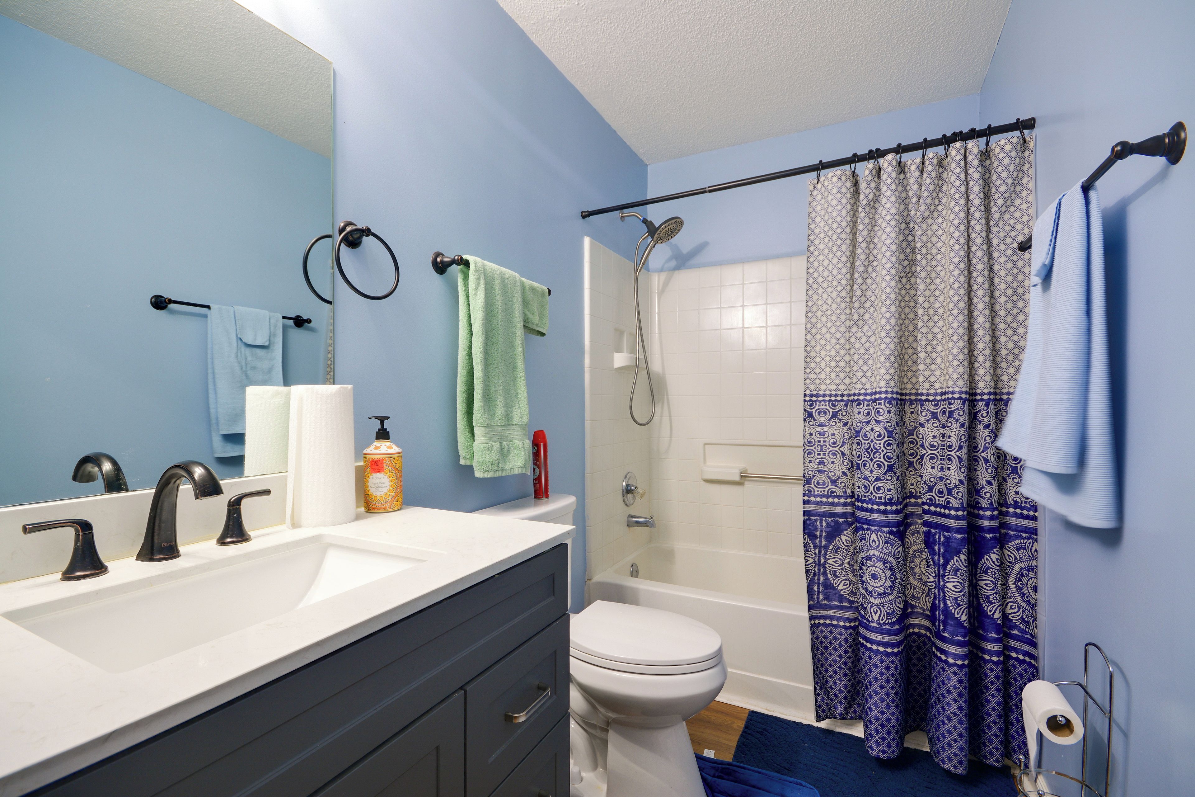 A bathroom with a white sink, two faucets, a toilet, a shower with a patterned curtain, and a mirror.
