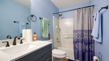 A bathroom with a white sink, two faucets, a toilet, a shower with a patterned curtain, and a mirror.