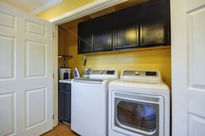A laundry room with two washing machines and a dryer, a black cabinet above, and a door on the left.