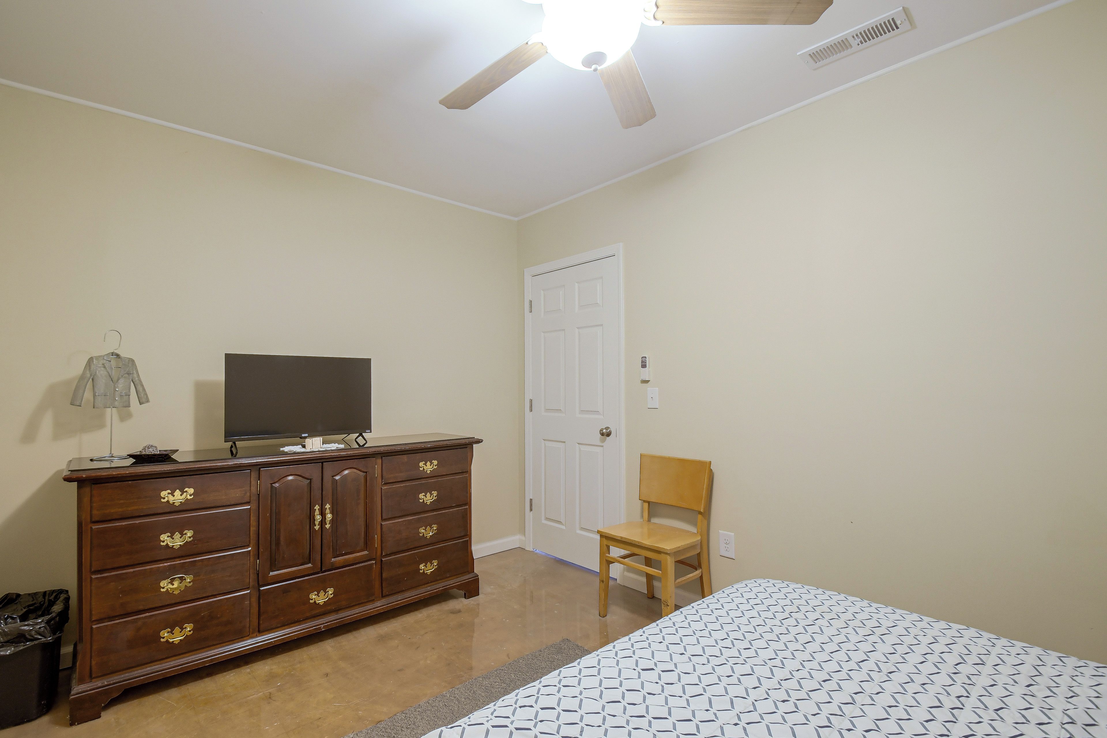A bedroom with a bed, a dresser, a chair, a television, and a ceiling fan.