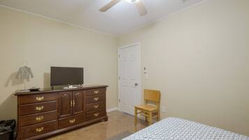 A bedroom with a bed, a dresser, a chair, a television, and a ceiling fan.
