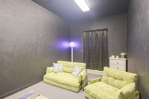 A room with a sofa, two armchairs, a floor lamp, a dresser, and a window with curtains.