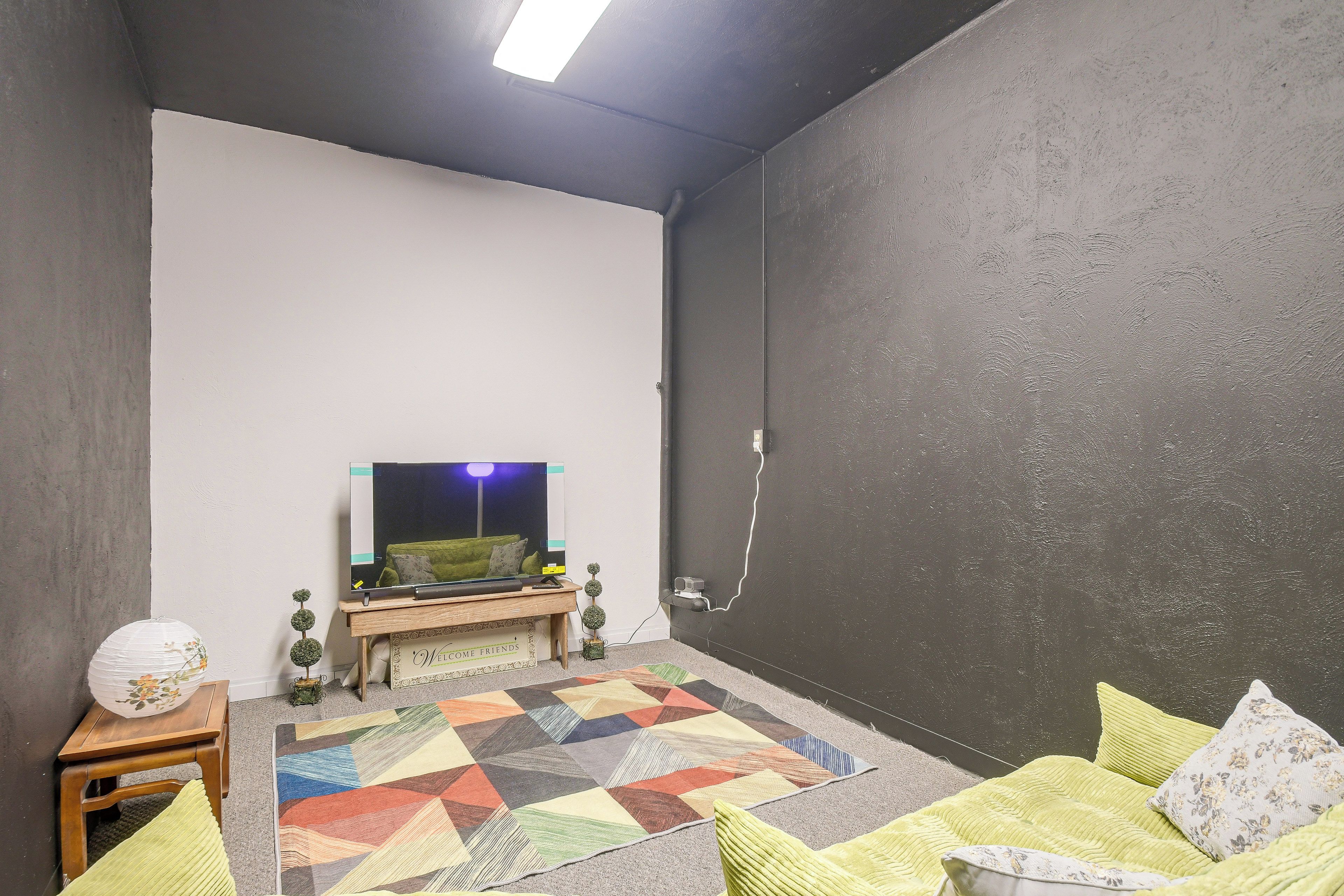A room with a television on a stand, a patterned rug, and a couch with pillows.