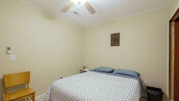 A bedroom with a bed, a chair, a bedside table, a ceiling fan, and a wall-mounted light fixture.
