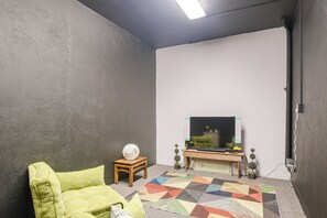 A room with a television on a wooden stand, a patterned rug, and a green sofa.
