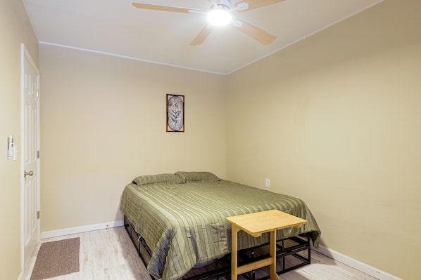 A bedroom with a single bed, a small table, a ceiling fan, and a wall-mounted picture.