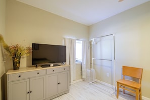 Habitación con una televisión sobre un mueble, una silla, una ventana con cortinas y una zona de ducha.