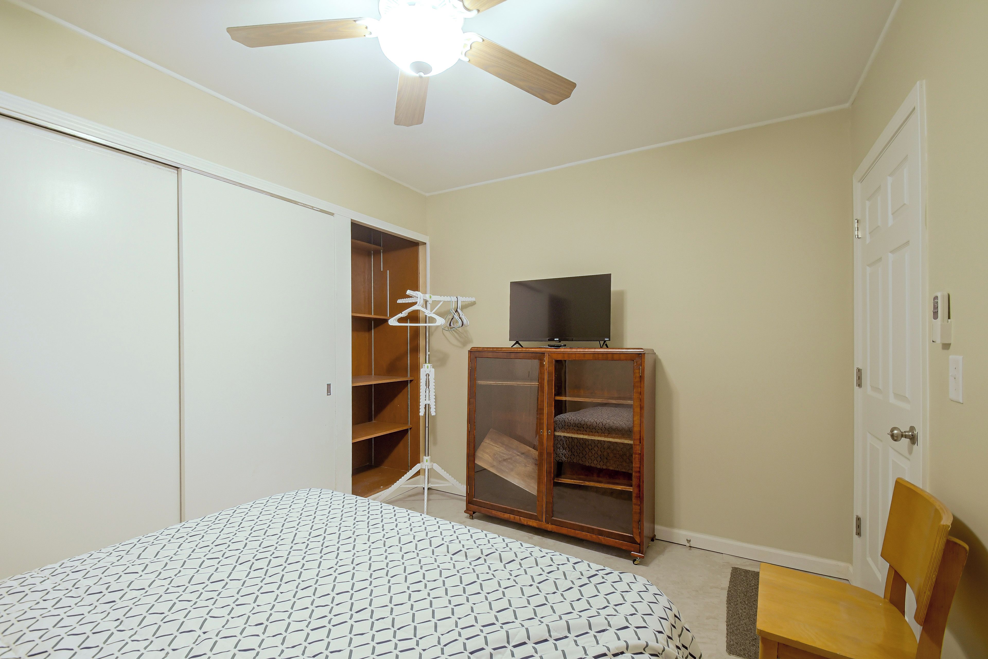 A bedroom with a bed, a wardrobe, a television on a stand, and a chair.