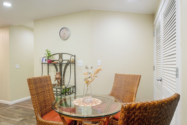 Un comedor con una mesa redonda de vidrio, sillas de mimbre, un reloj de pared y una estantería con objetos decorativos.