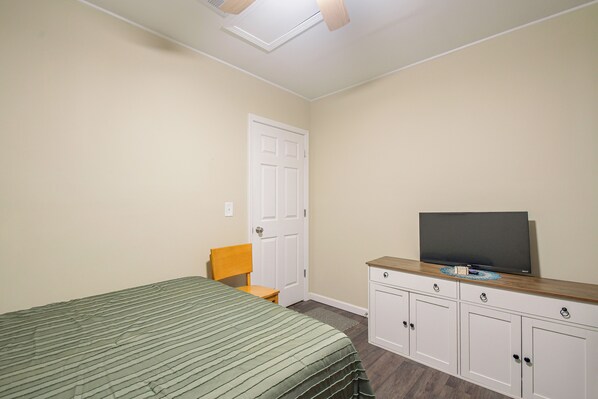 A bedroom with a bed, a chair, a television on a cabinet, and a door.
