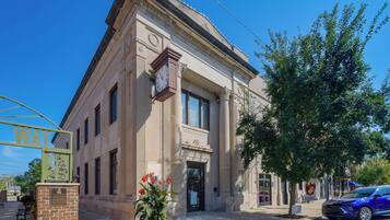 A classical building with a clock, a bench, and a tree in front.