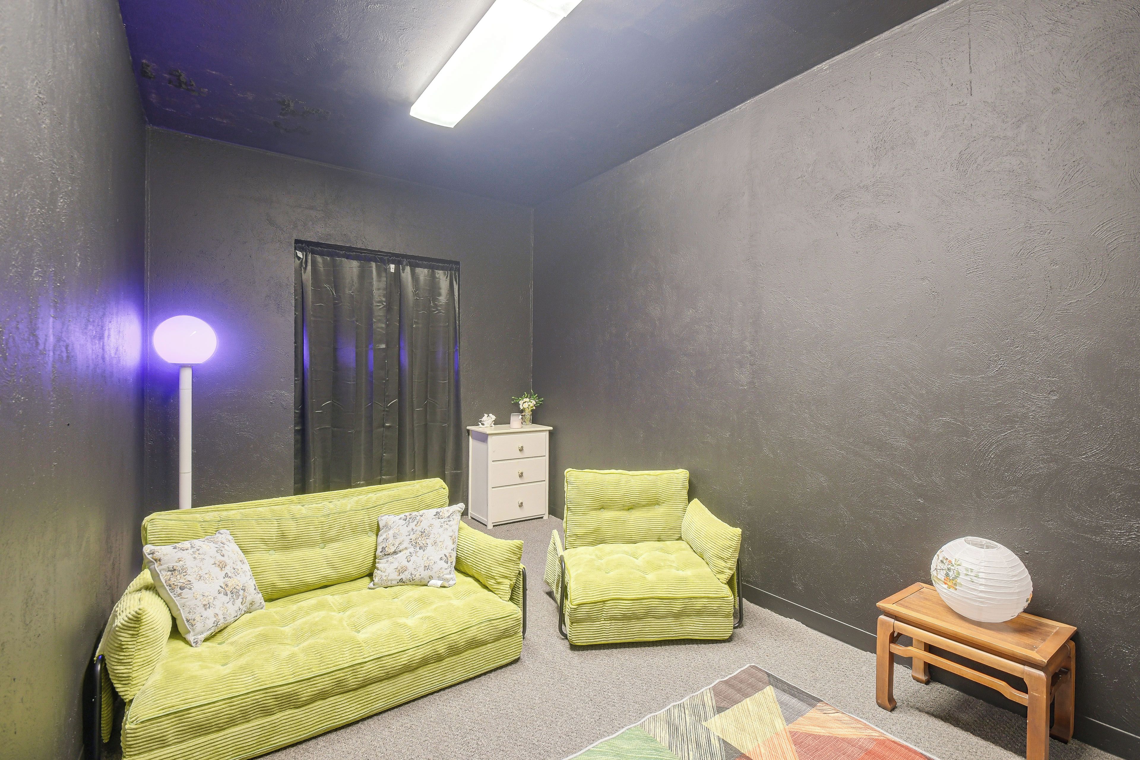 A room with a green sofa set, a white dresser, a small wooden table with a decorative item, and a floor lamp.