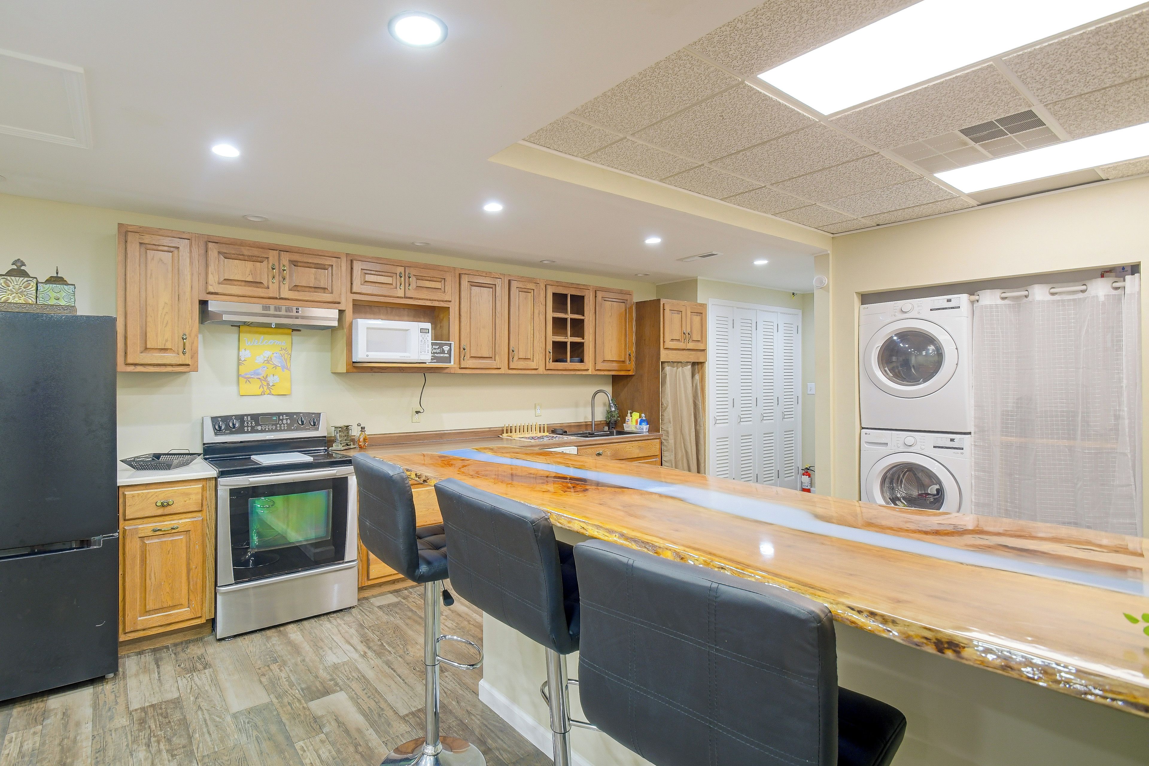 A kitchen with wooden cabinets, a microwave, a stove, a sink, and a bar area with chairs.