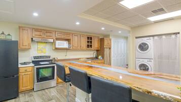 A kitchen with wooden cabinets, a microwave, a stove, a sink, and a bar area with chairs.