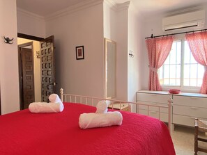 A bedroom with a red bedspread, a white dresser, a mirror, and a window with pink curtains. - Apartment in Nerja With Sea Views & Pool (Nerja)