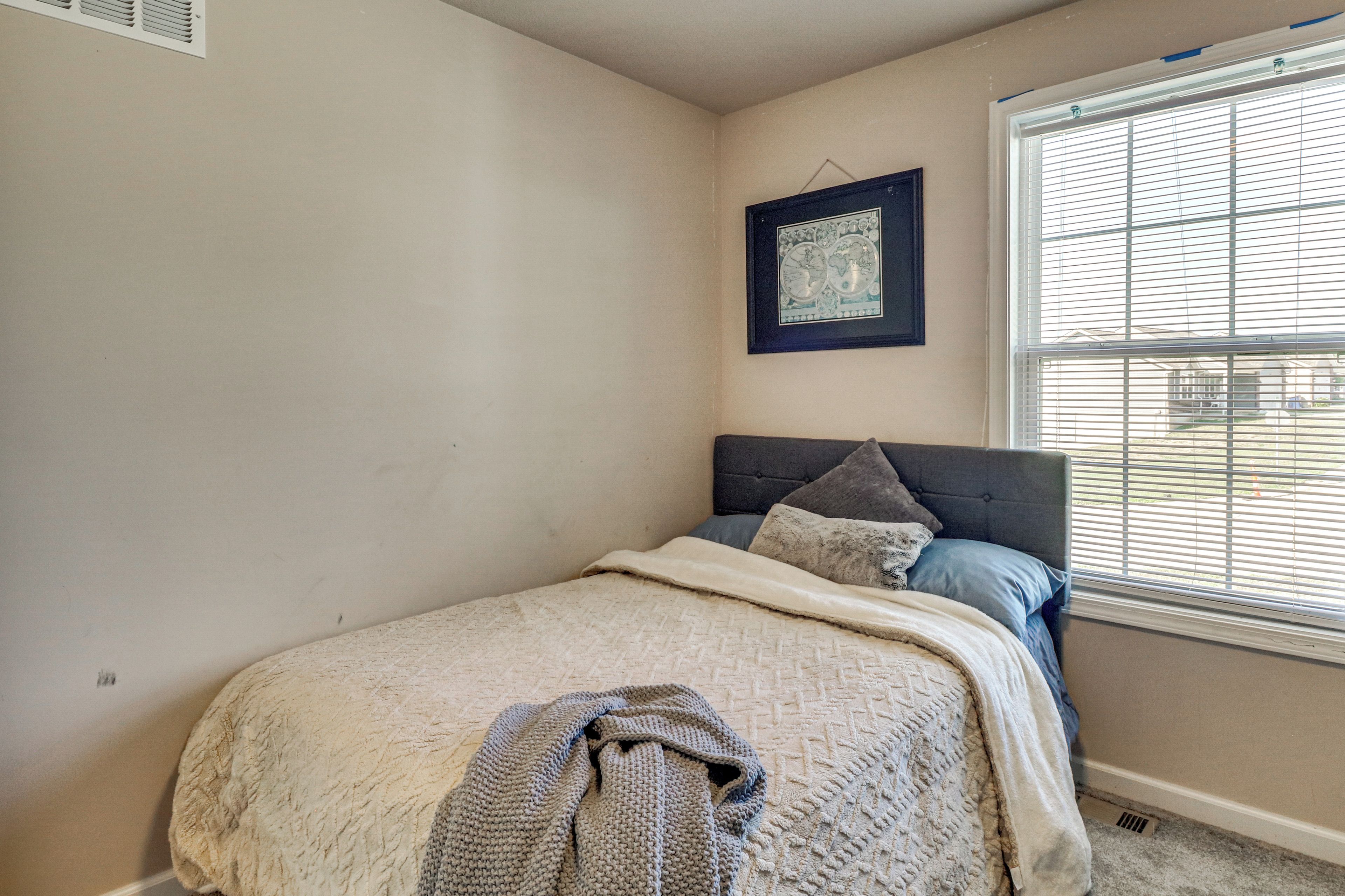 Une chambre à coucher avec un lit, une fenêtre avec des stores et un tableau encadré au mur.
