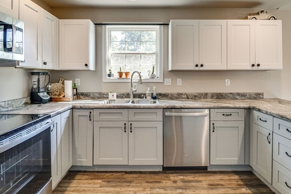 A kitchen with white cabinets, a stainless steel dishwasher, and a window with plants.