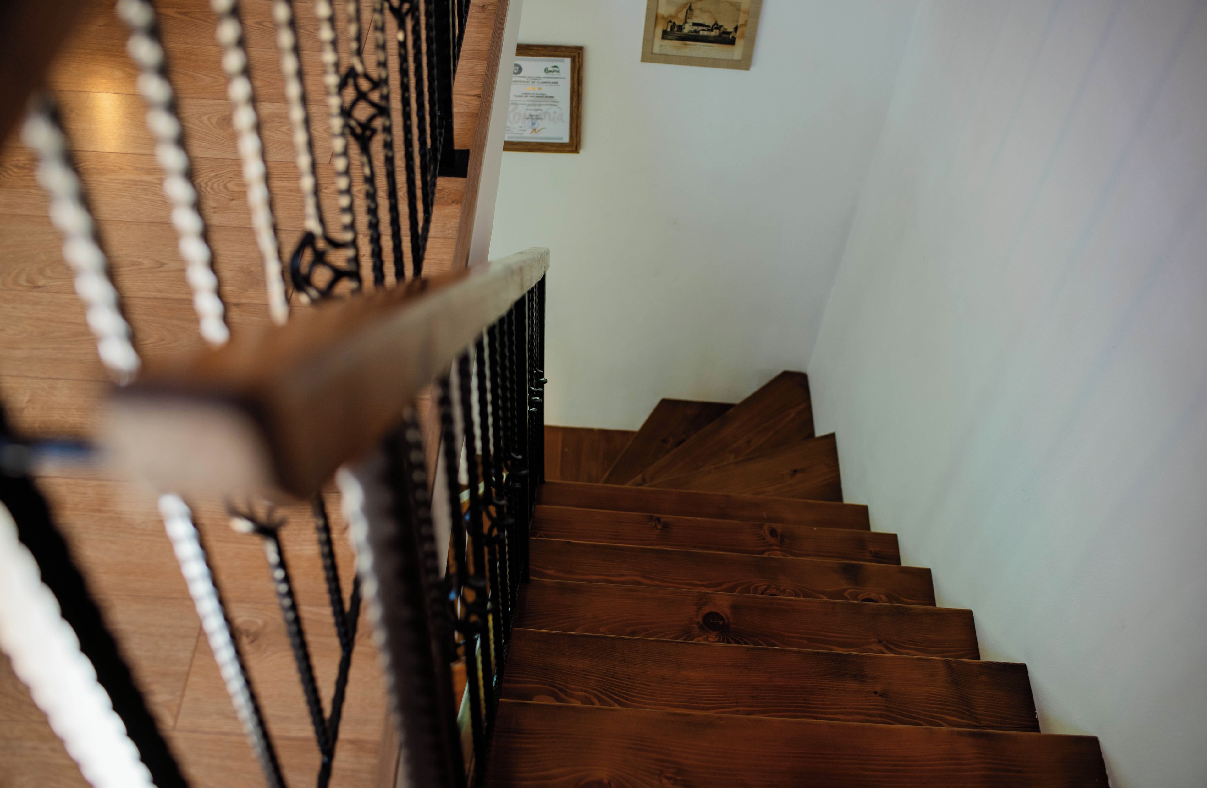 A wooden staircase with a handrail, a wall-mounted certificate, and a framed picture.