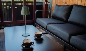 A room with a black leather sofa, a table with two cups of coffee, and a green lamp.