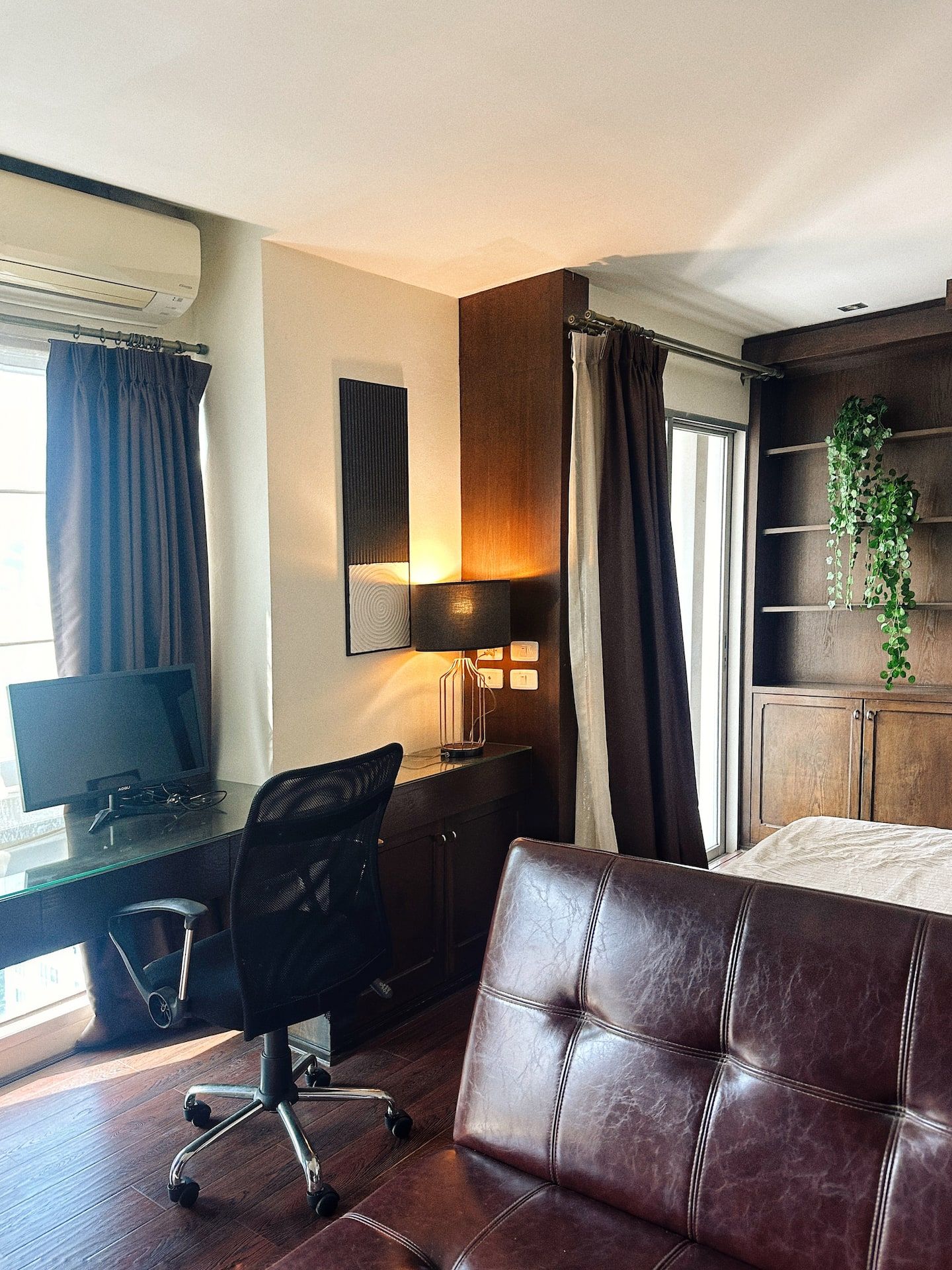 A hotel room with a desk, chair, bed, and a plant.
