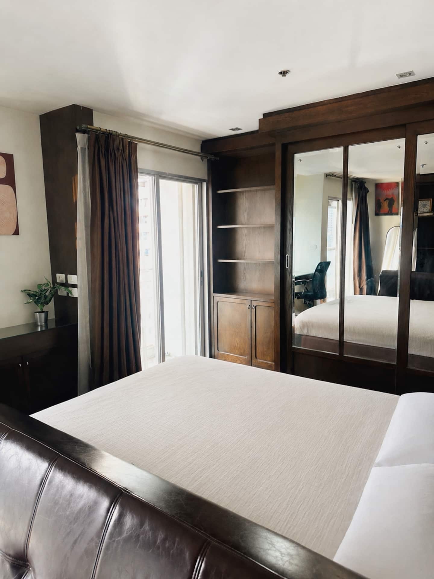 A hotel room with a bed, a desk, a chair, a wardrobe, and a potted plant.