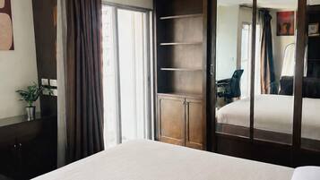 A hotel room with a bed, a desk, a chair, a wardrobe, and a potted plant.